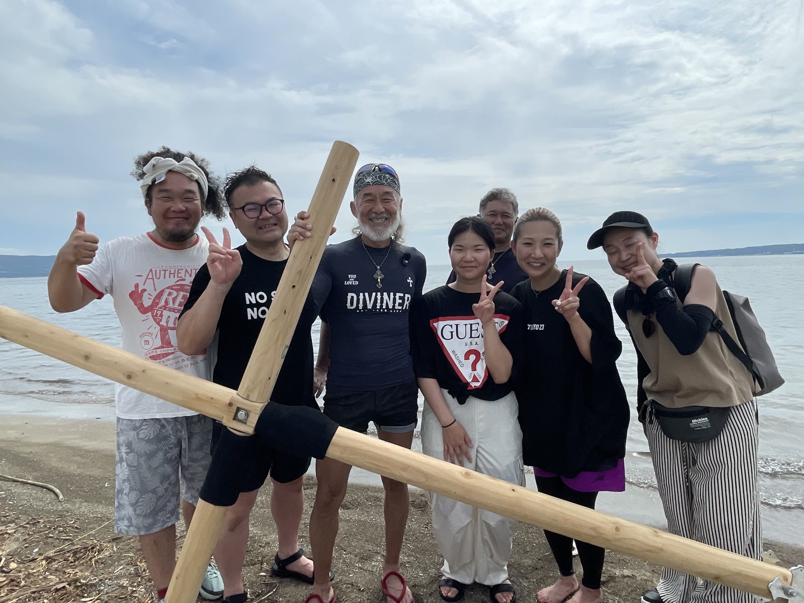 洗礼後に佐渡の海を背に十字架を囲む片山さんご一家と仲間たち