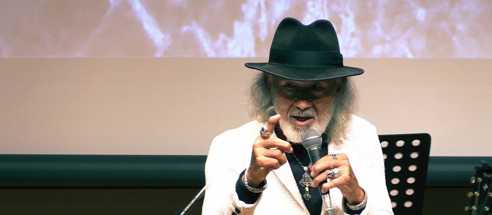 会場でマイクを持ち、指を差しながら語るアーサー・ホーランズ
