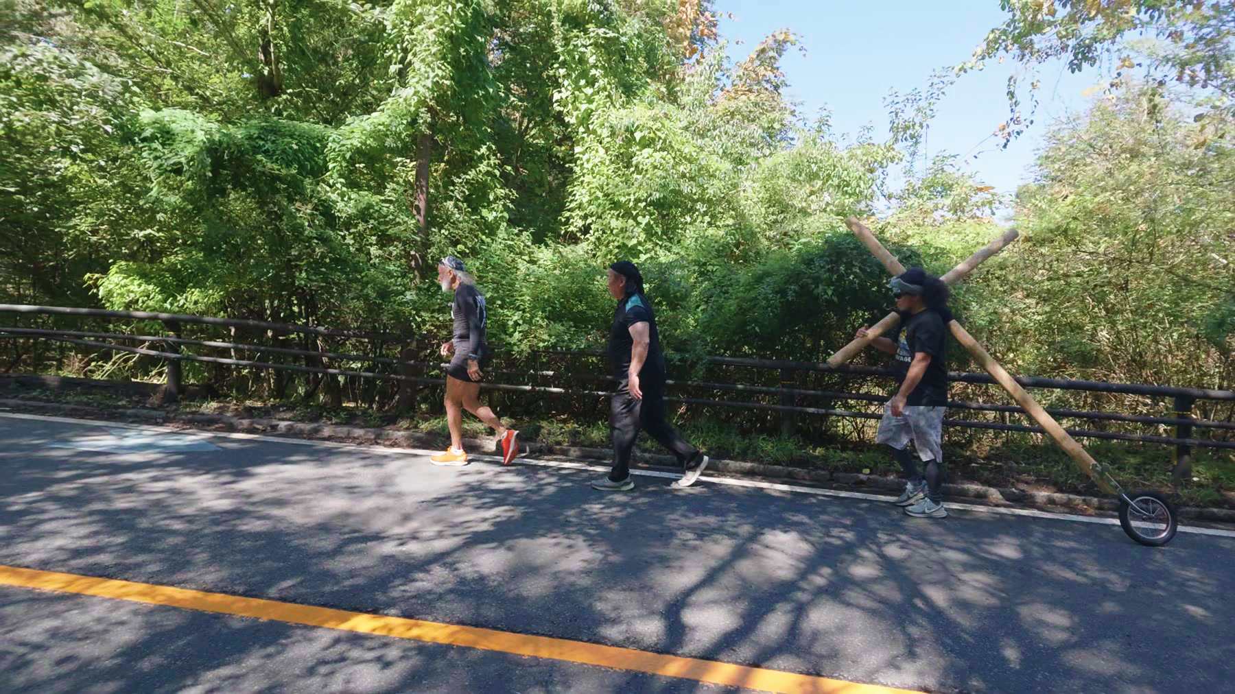 木立沿いの道路で十字架を運ぶアーサー先生と同行者たち