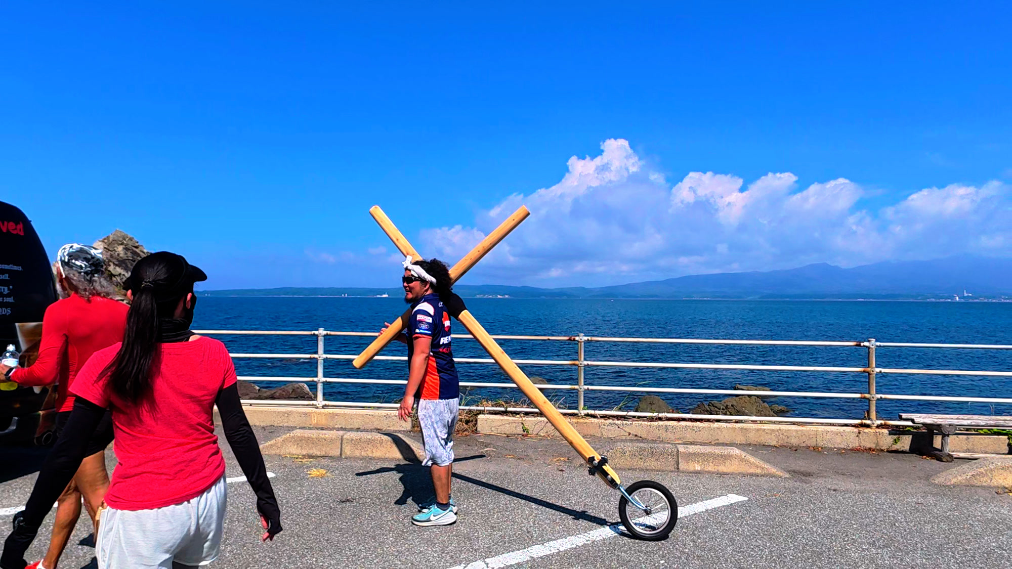佐渡の海沿いを十字架とともに歩く複数の参加者