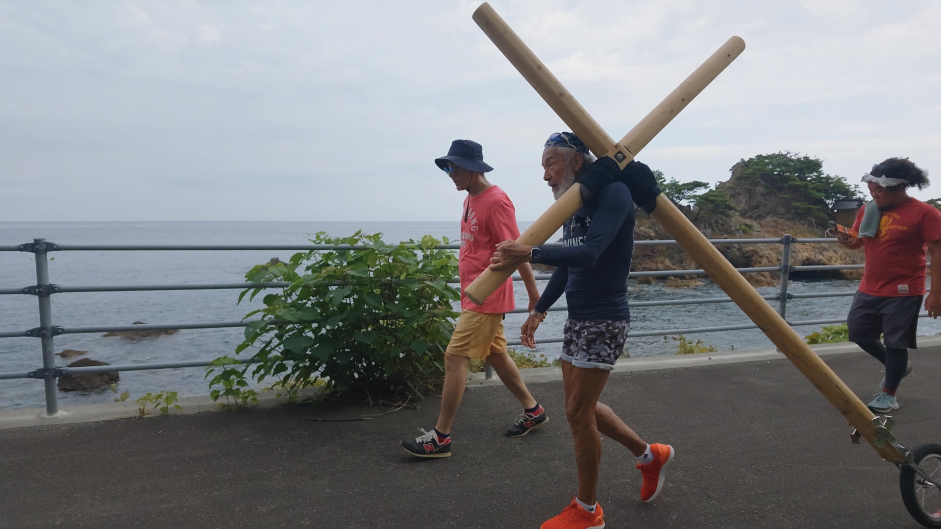 青い海を背に、十字架を担ぐアーサー先生と同行者たち